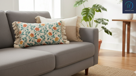 Gezellige woonkamer met grijze bank, sierkussens met bloemen en franjes, plant en houten tafel voor frisse, stijlvolle sfeer.