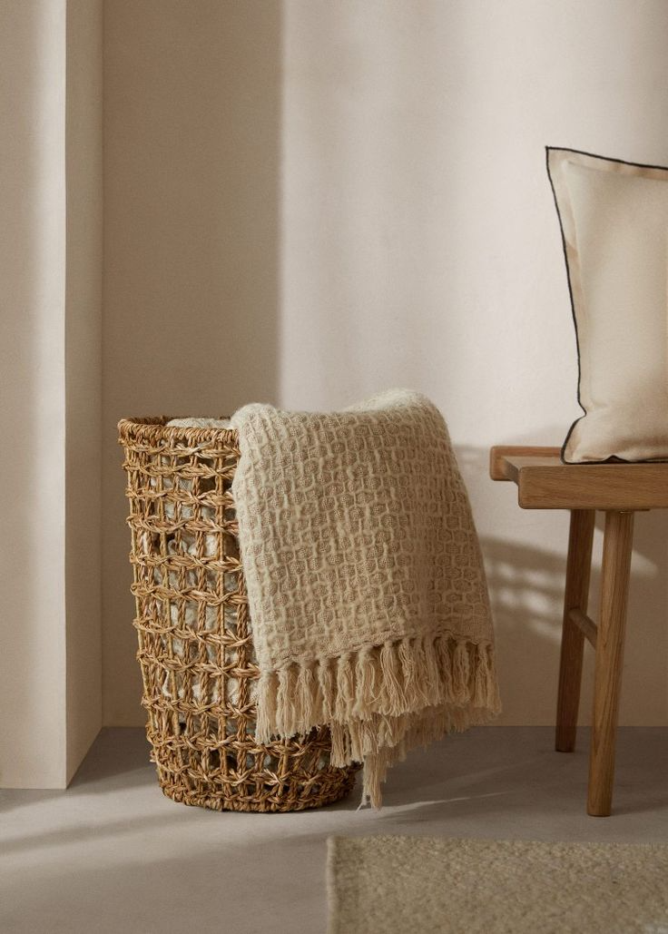 Cozy scene with beige textured blanket on wicker basket, wooden bench with neutral cushion, warm home decor